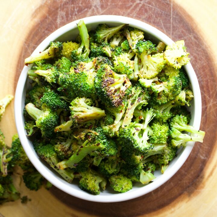 A bowl of sautéd broccoli on a wood cutting board.