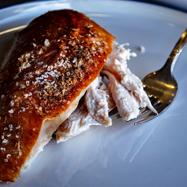 A slice of perfect roast chicken on a plate with a fork.
