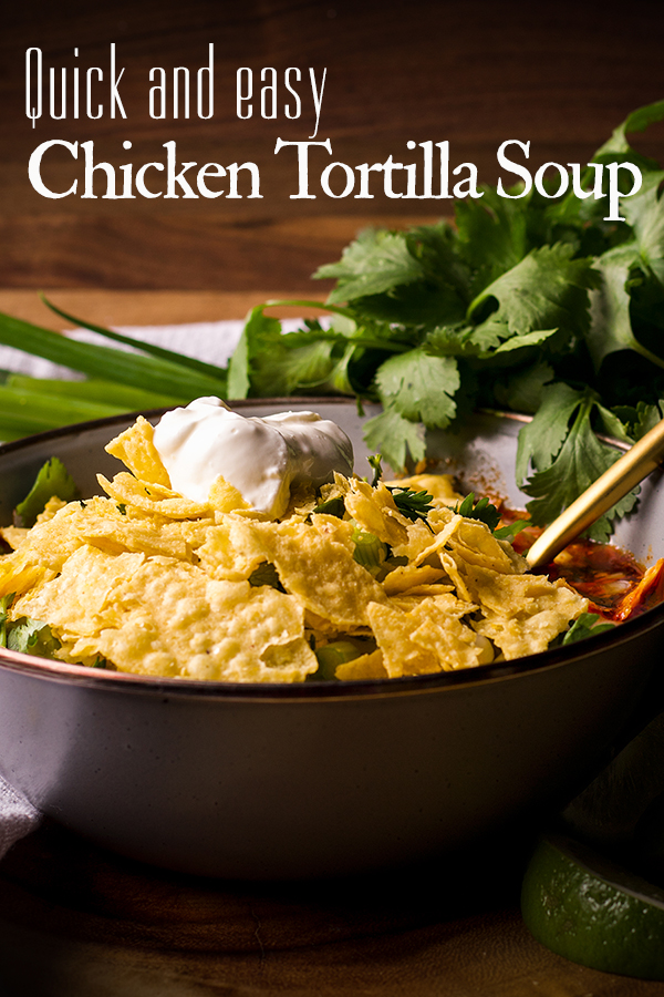 A bowl of chicken tortilla soup topped with crushed tortilla chips and sour cream.
