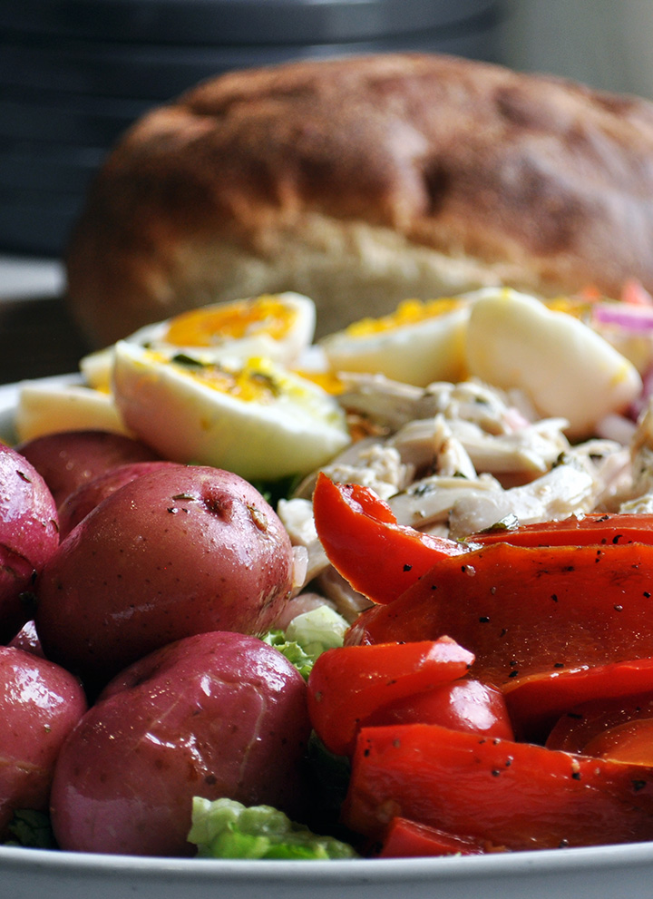 Boiled red potatoes and roasted red peppers are arranged on a chicken nicoise salad.