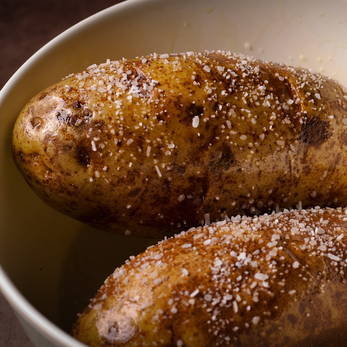 Two Russet potatoes in a bowl covered with olive oil and salt.
