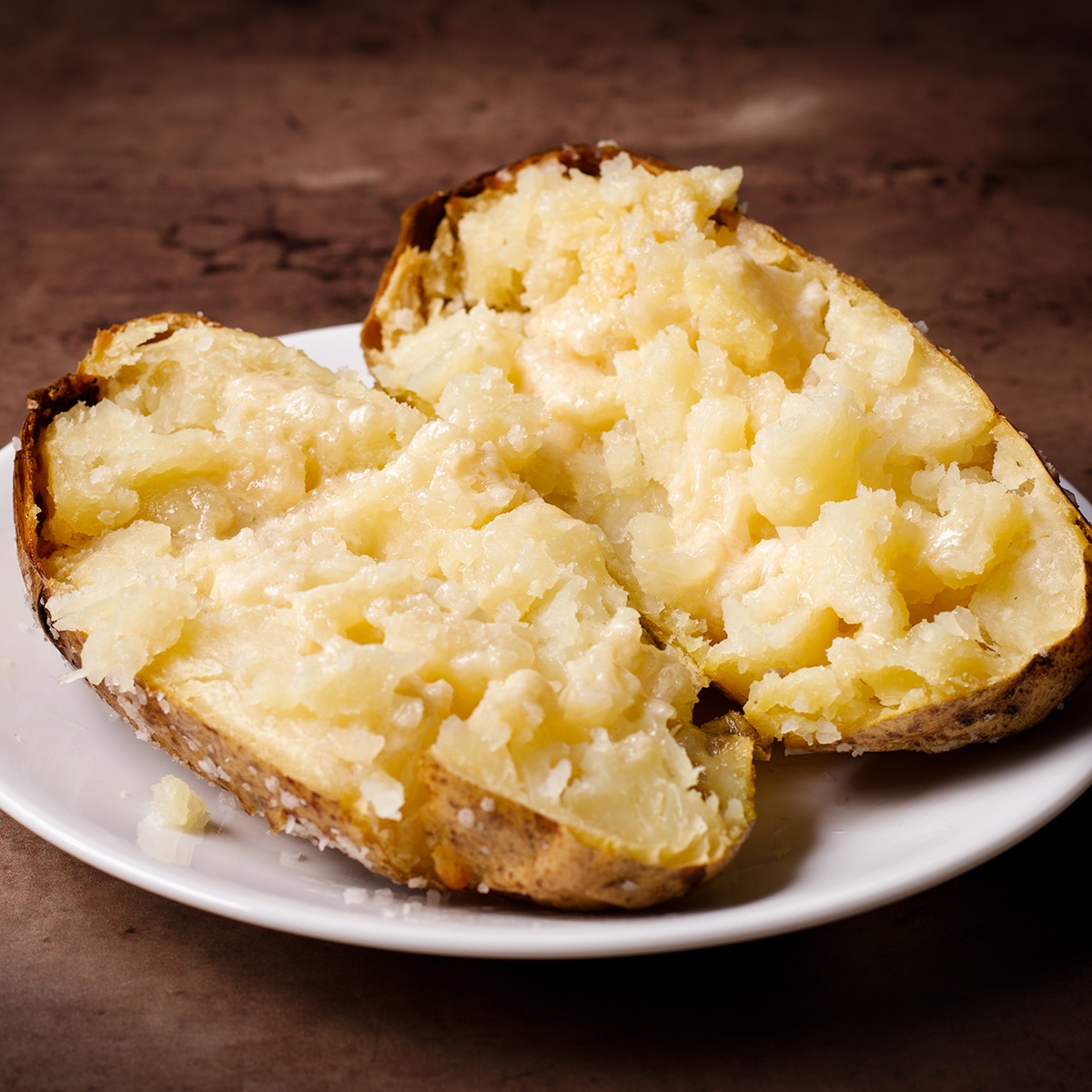 A hot baked potato on a white plate, split in half and ready to eat.