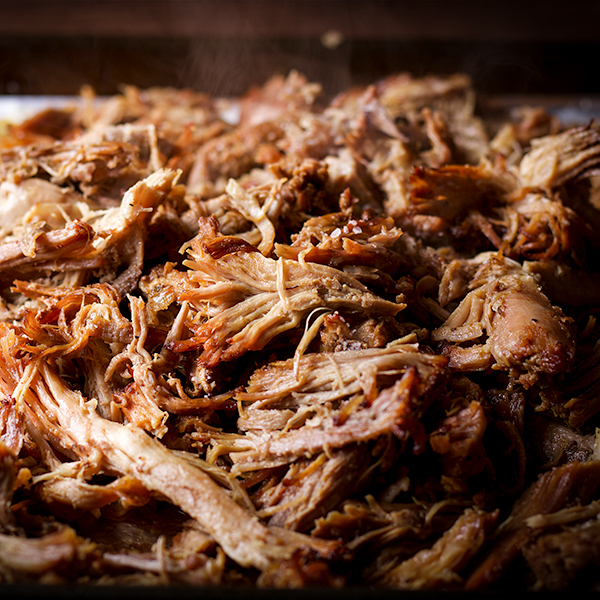 A tray of crispy and tender carnitas, hot from the oven, with steam rising from them.