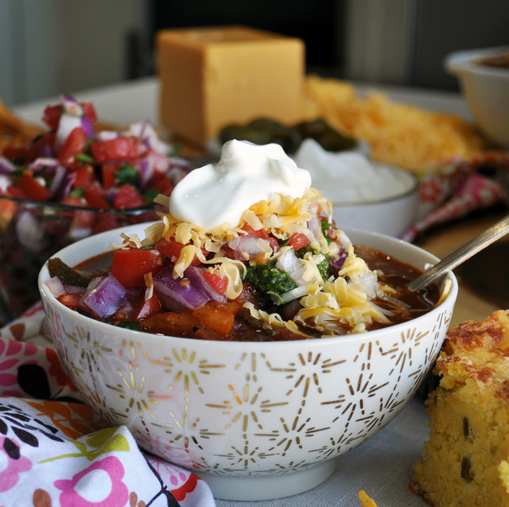 A bowl of vegetarian chili topped with Pico de Gallo, chimichurri sauce, cheese, and sour cream.