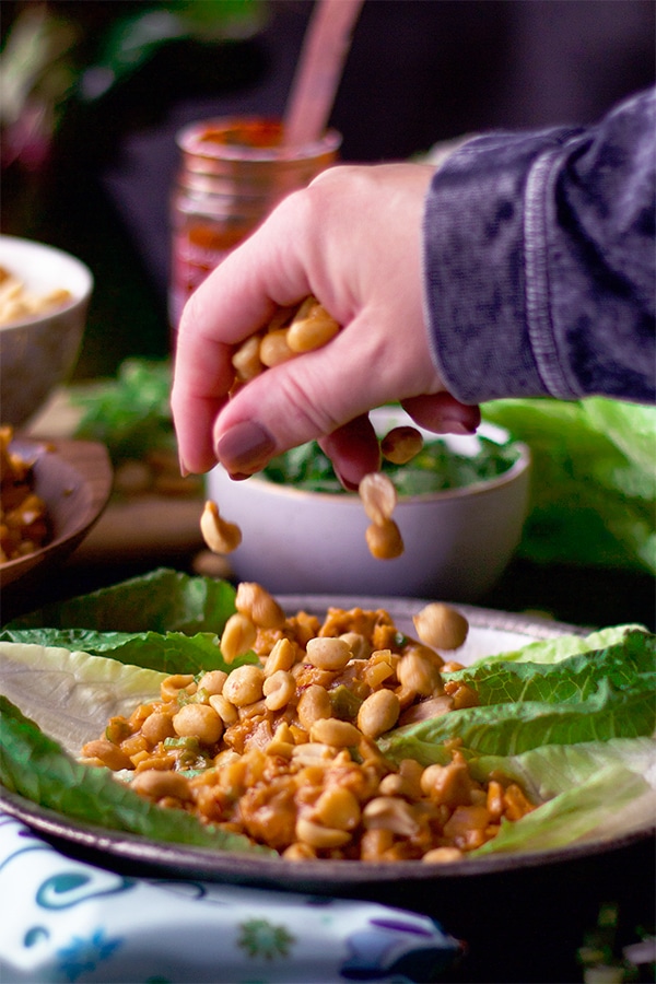 Sprinkling peanuts over chicken lettuce wraps.