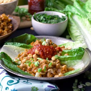A plate of chicken lettuce wraps with peanuts and chili garlic sauce.
