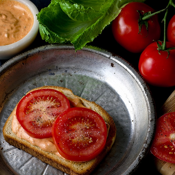 How to build a BLT Sandwich: spread with special sauce and add fresh tomatoes.