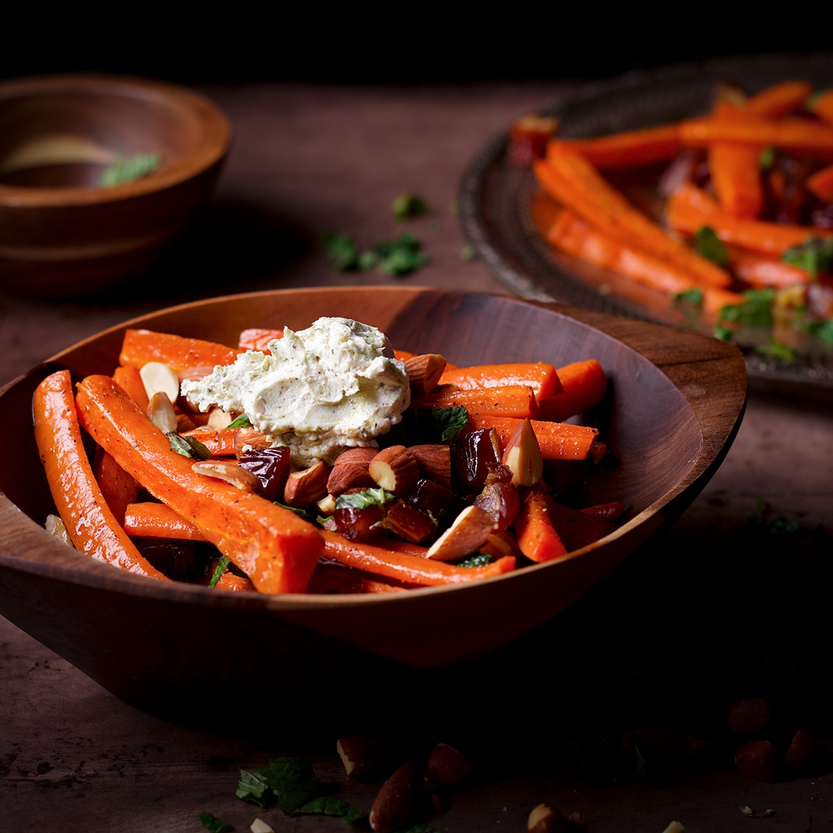 A wood bowl filled with roasted carrots and dates that have been topped with a dollop of homemade labneh.