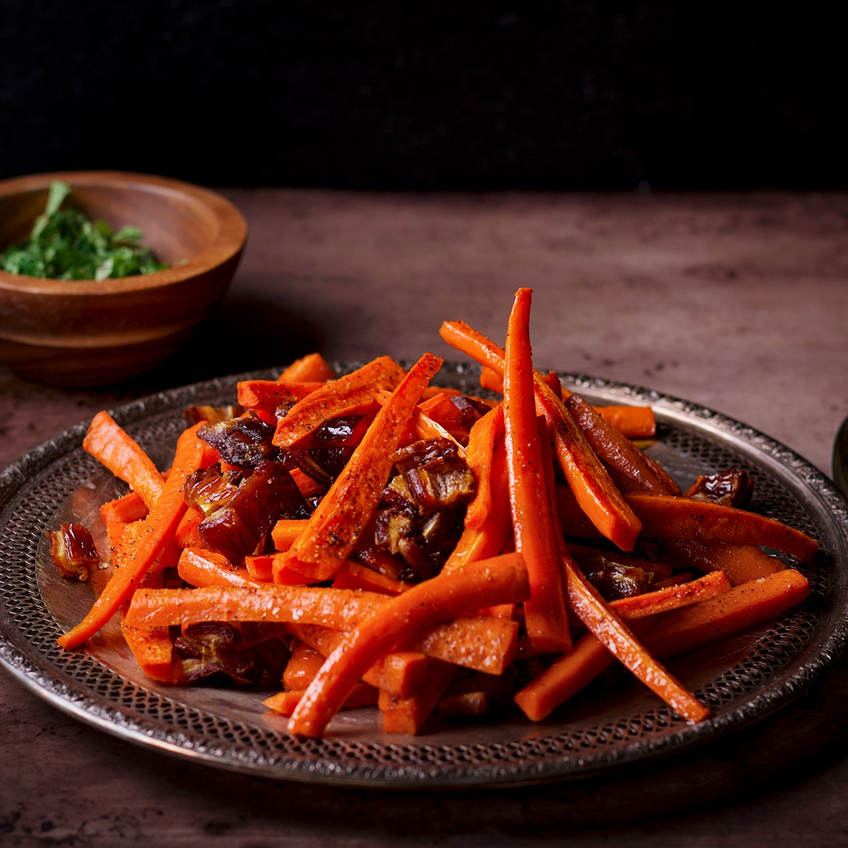 A silver platter piled high with roasted carrots and dates.