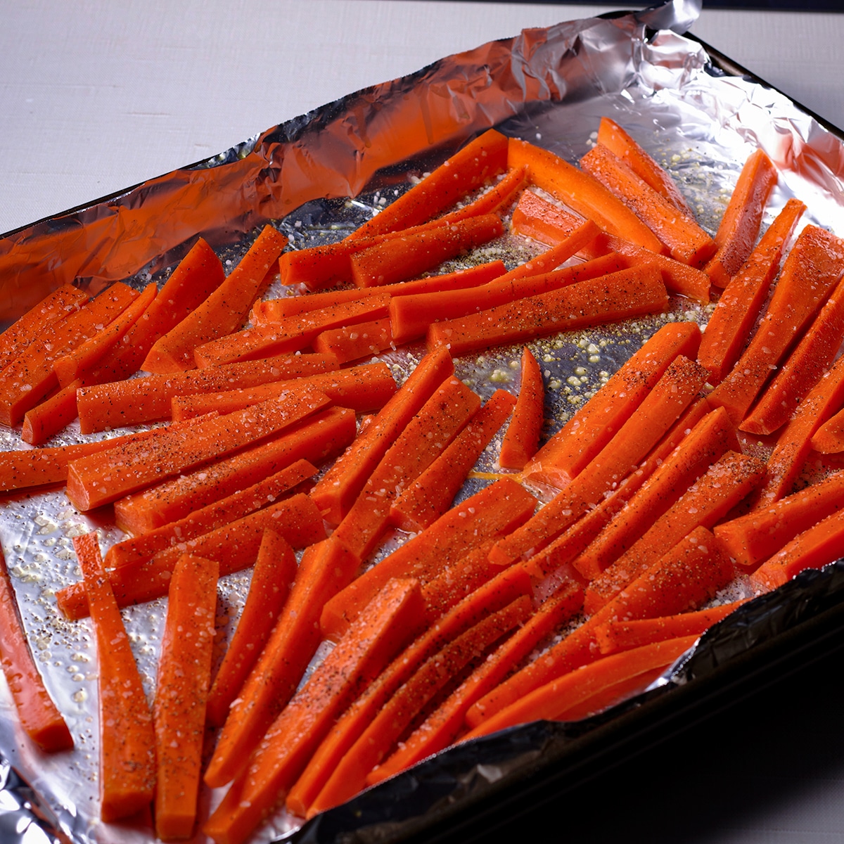 Carrots tossed in olive oil and sprinkled with salt and pepper on a foil lined baking sheet.
