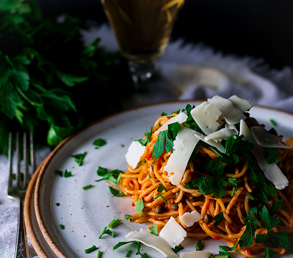 A plate of Spaghetti Puttanesca topped with parsley and shaved parmesan.