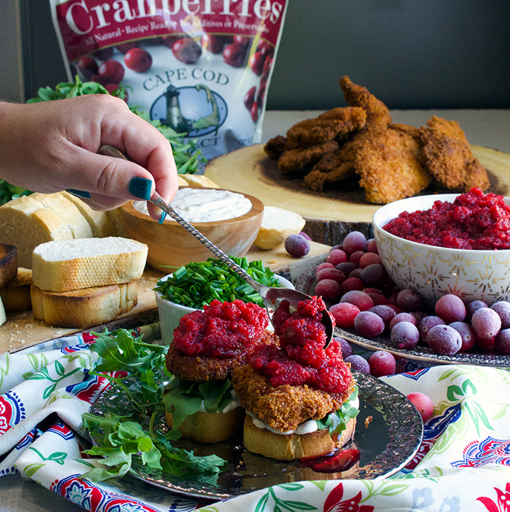 Spooning spicy cranberry relish over Fried chicken sandwiches with savory mayonnaise, arugula, and spicy cranberry relish.