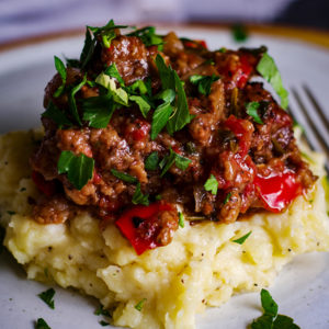 A plate of garlic mascarpone mashed potatoes topped with Tuscan Braised Beef and fresh parsley.