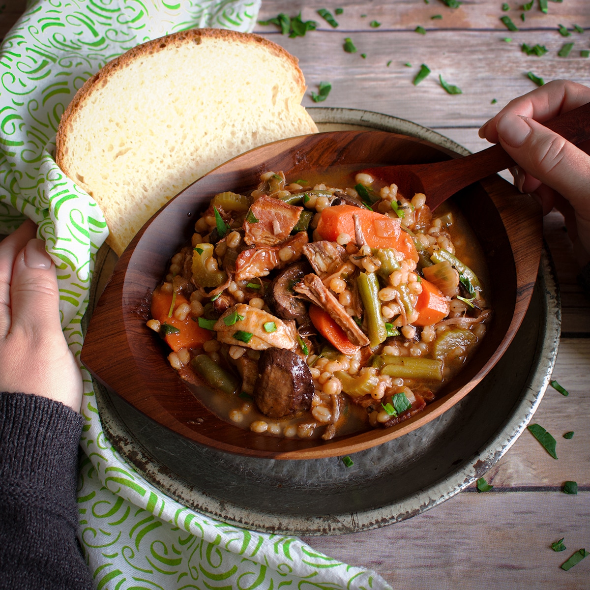A wood bowl filled with homemade beef and barley soup.