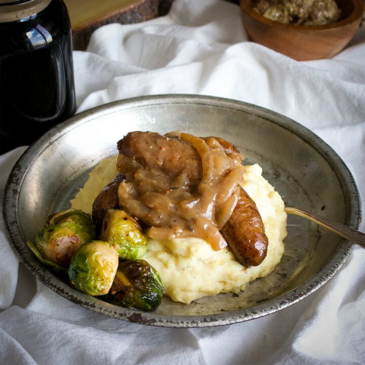 A tin plate filled with cream cheese mashed potatoes and sausages covered in onion gravy.