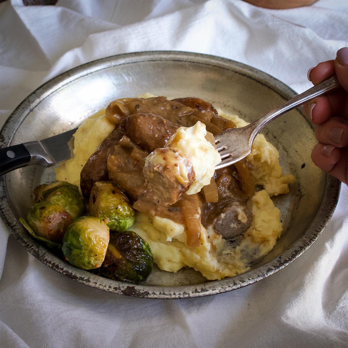 Someone using a fork to lift a bite of bangers and mash.
