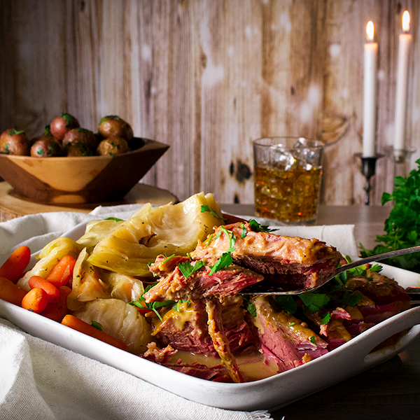 A platter on a table with corned beef and cabbage with mustard sauce and parsley buttered potatoes.