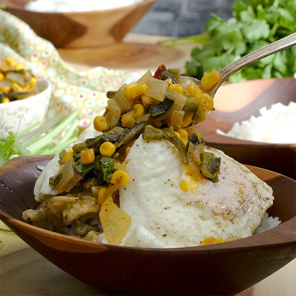 Spooning roasted corn salsa over Tomatillo Pulled Chicken and Rice Bowls with fried eggs