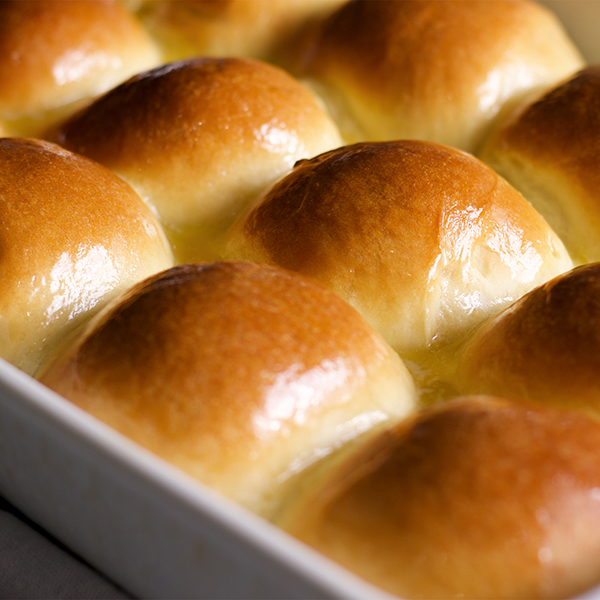 A pan of homemade dinner rolls slathered in melted butter, ready to serve.
