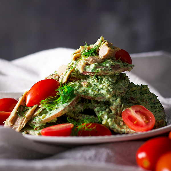 A plate of potato salad with creamy avocado and herb green sauce, tuna fillets and tomatoes
