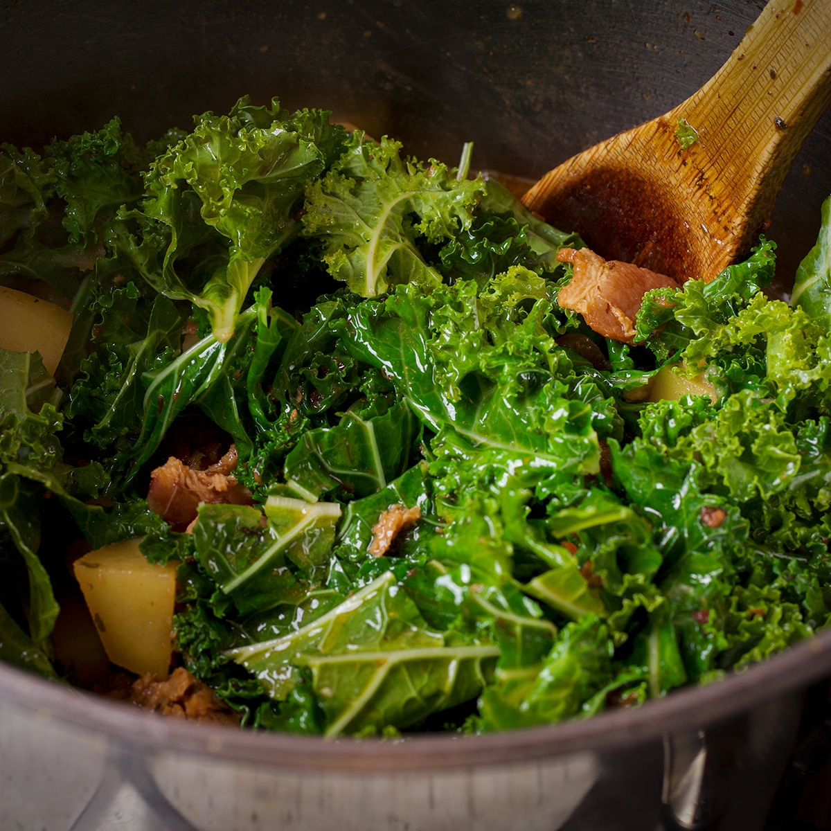 Adding chopped kale to the saucepan along with the cooked potatoes, sausage, and bacon.