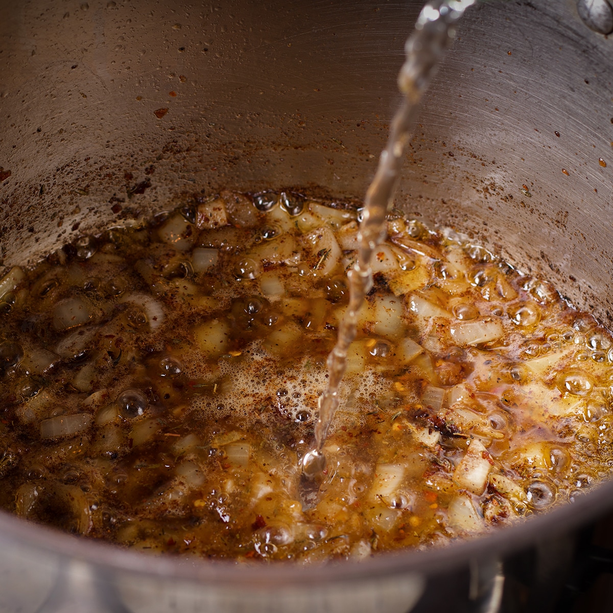 Pouring white wine into a saucepan with cooking onions, garlic, and spices.