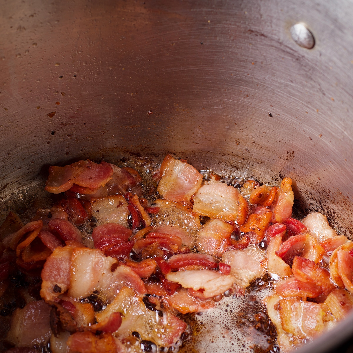 Pieces of thick cut bacon cooking in hot oil in a large saucepan. 
