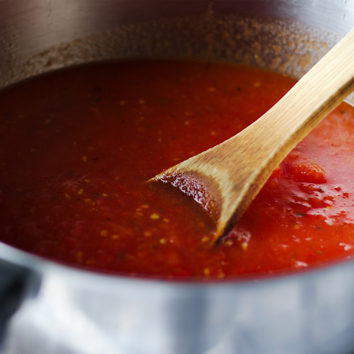 Using a wooden spoon to stir a pot of roasted tomato sauce while it simmers.