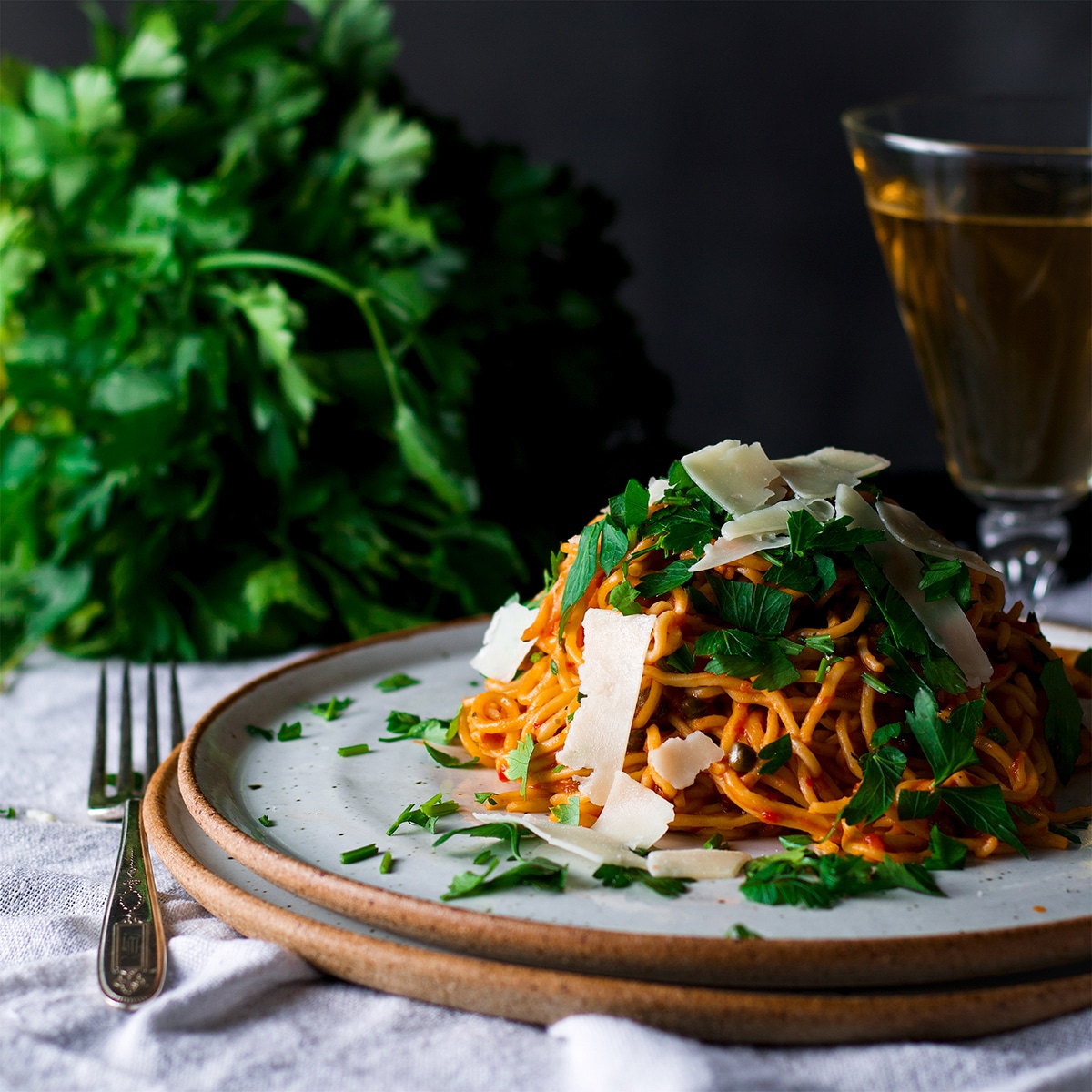 A serving of spaghetti puttanesca topped with shaved parmesan cheese and fresh Italian parsley.