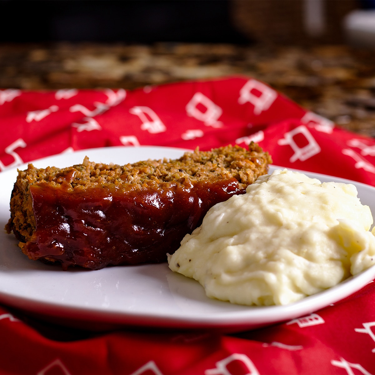 A slice of meatloaf and a pile of mashed potatoes on a white plate. 