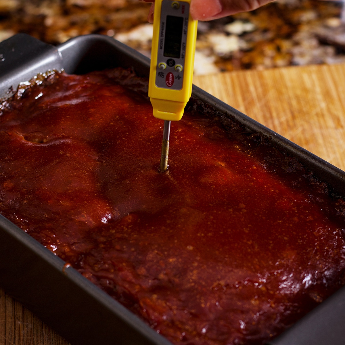 Sticking a meat thermometer in the center of a meatloaf to check its internal temperature.
