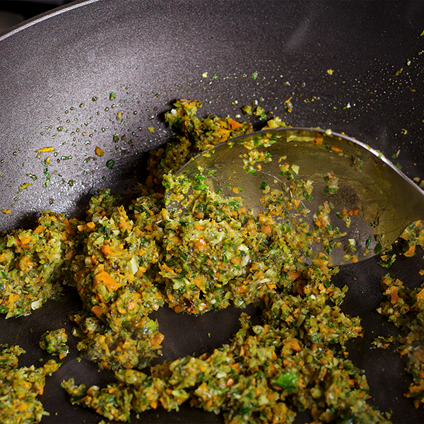 Someone cooking minced vegetables and herbs in a skillet. 