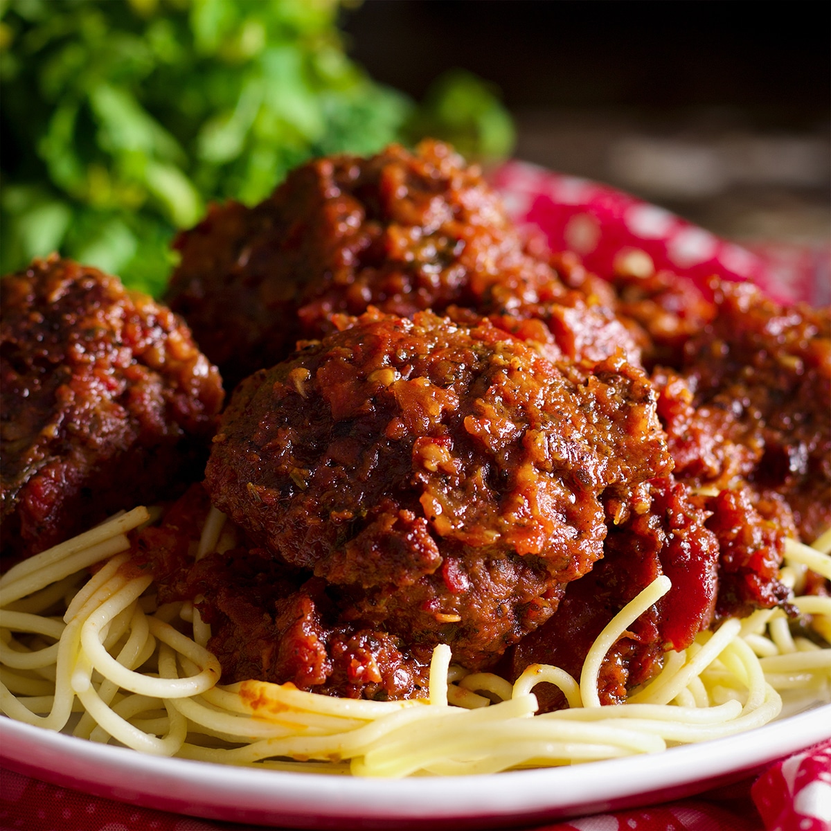 A plate piled high with spaghetti noodles topped with Italian meatballs baked in marinara.