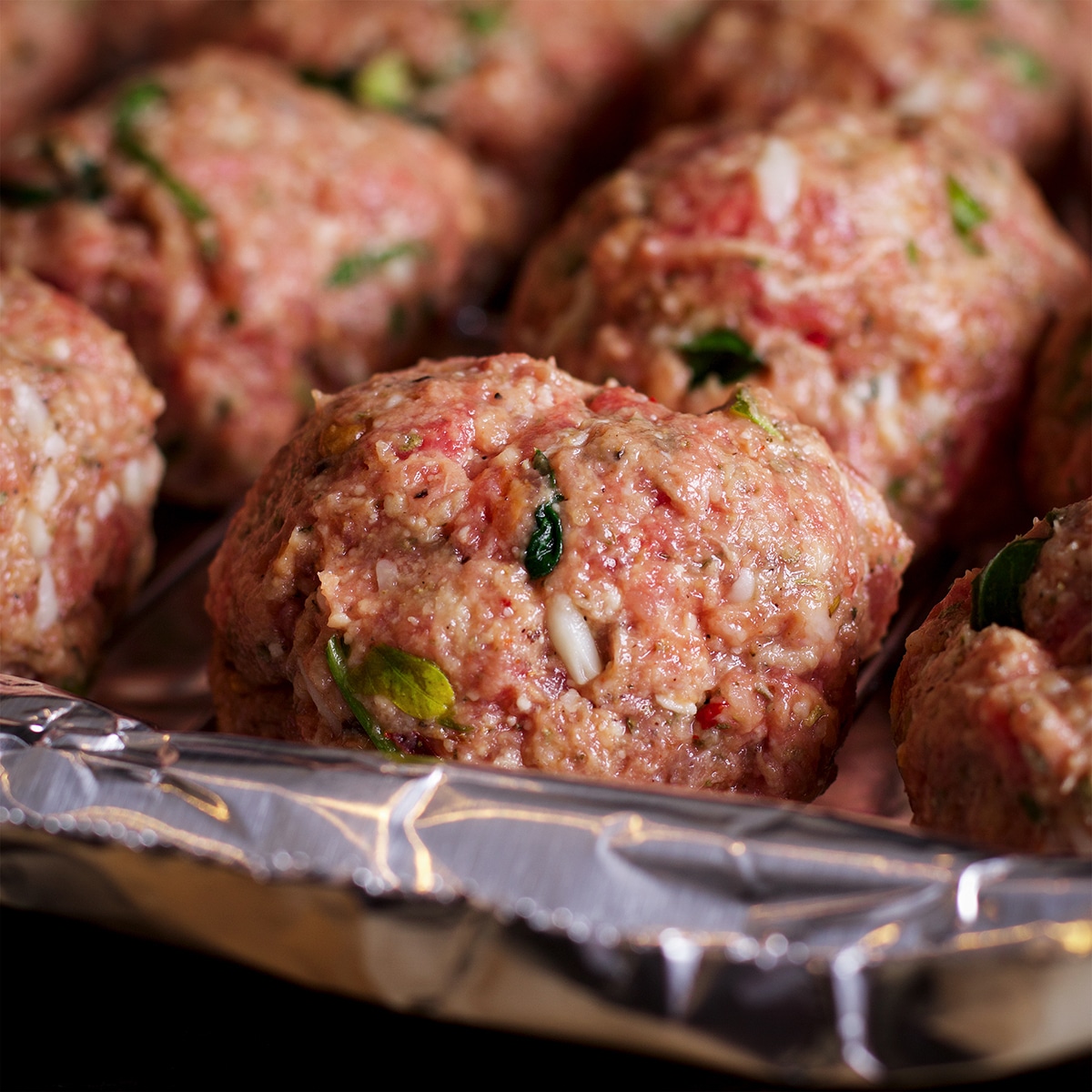 A broiling pan lined with foil containing raw Italian meatballs ready to go under the broiler to cook.