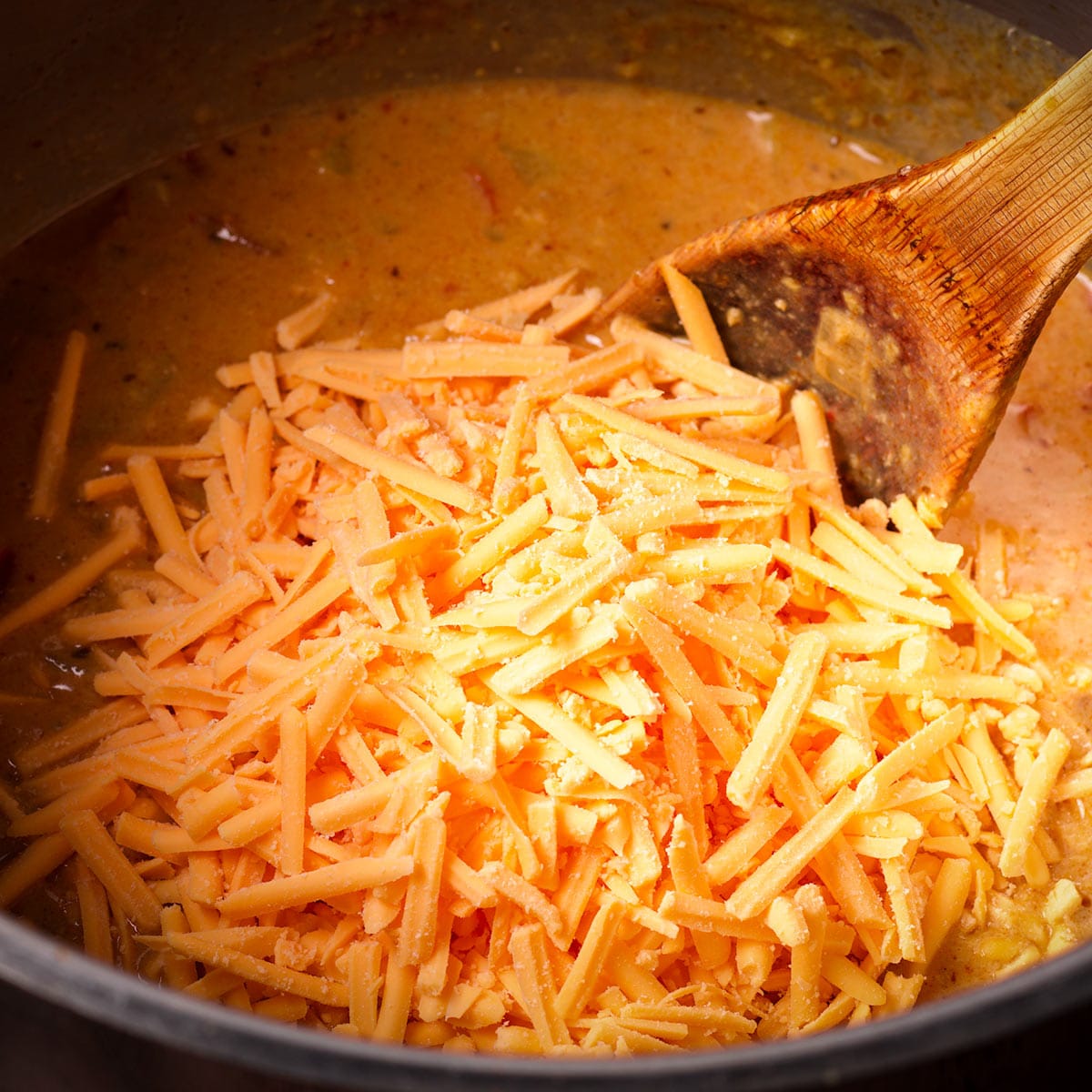 Add shredded cheddar cheese to the soup and stir until it's melted.