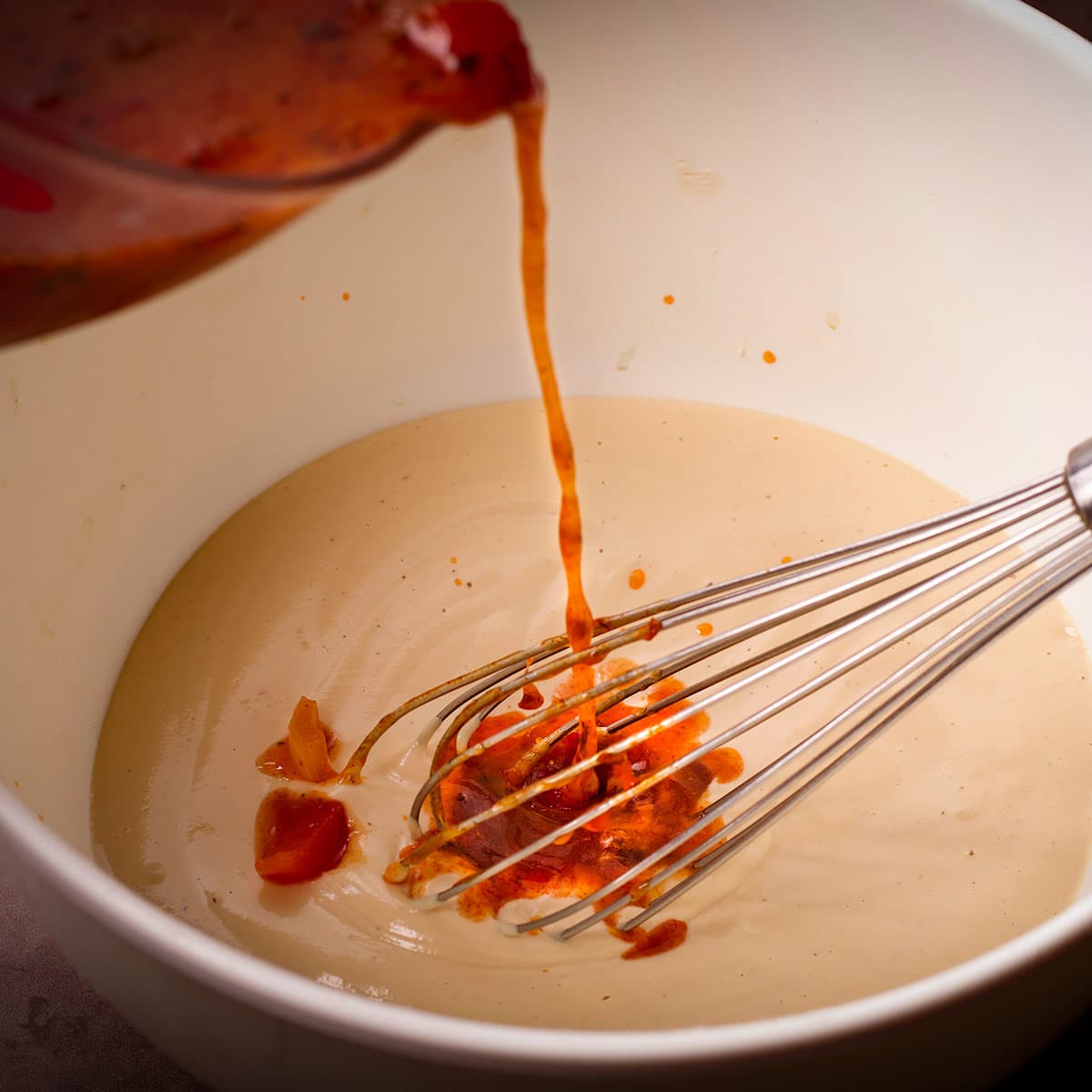 Pouring hot broth into sour cream while whisking.