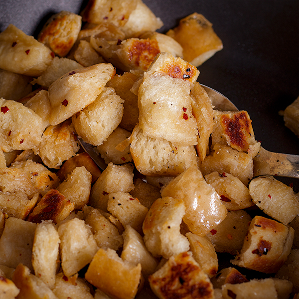 Homemade croutons being cooked in bacon fat in a hot skillet.