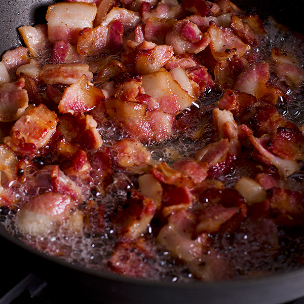 Pieces of bacon frying in a hot skillet. 