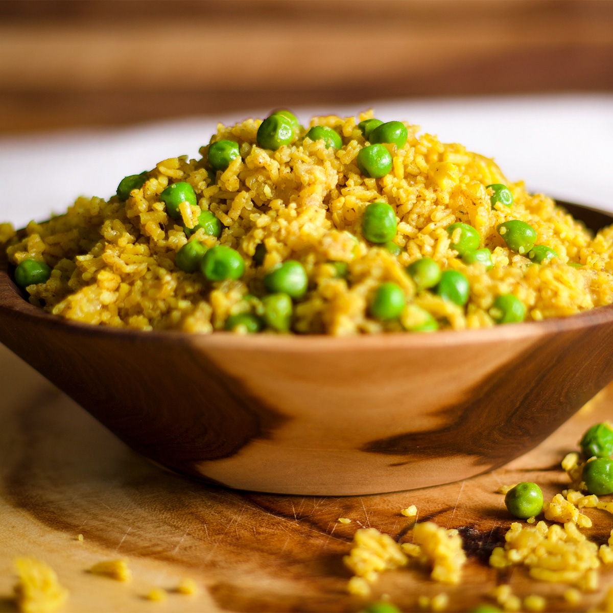 A wood bowl filled to overflowing with Indian Rice with peas.