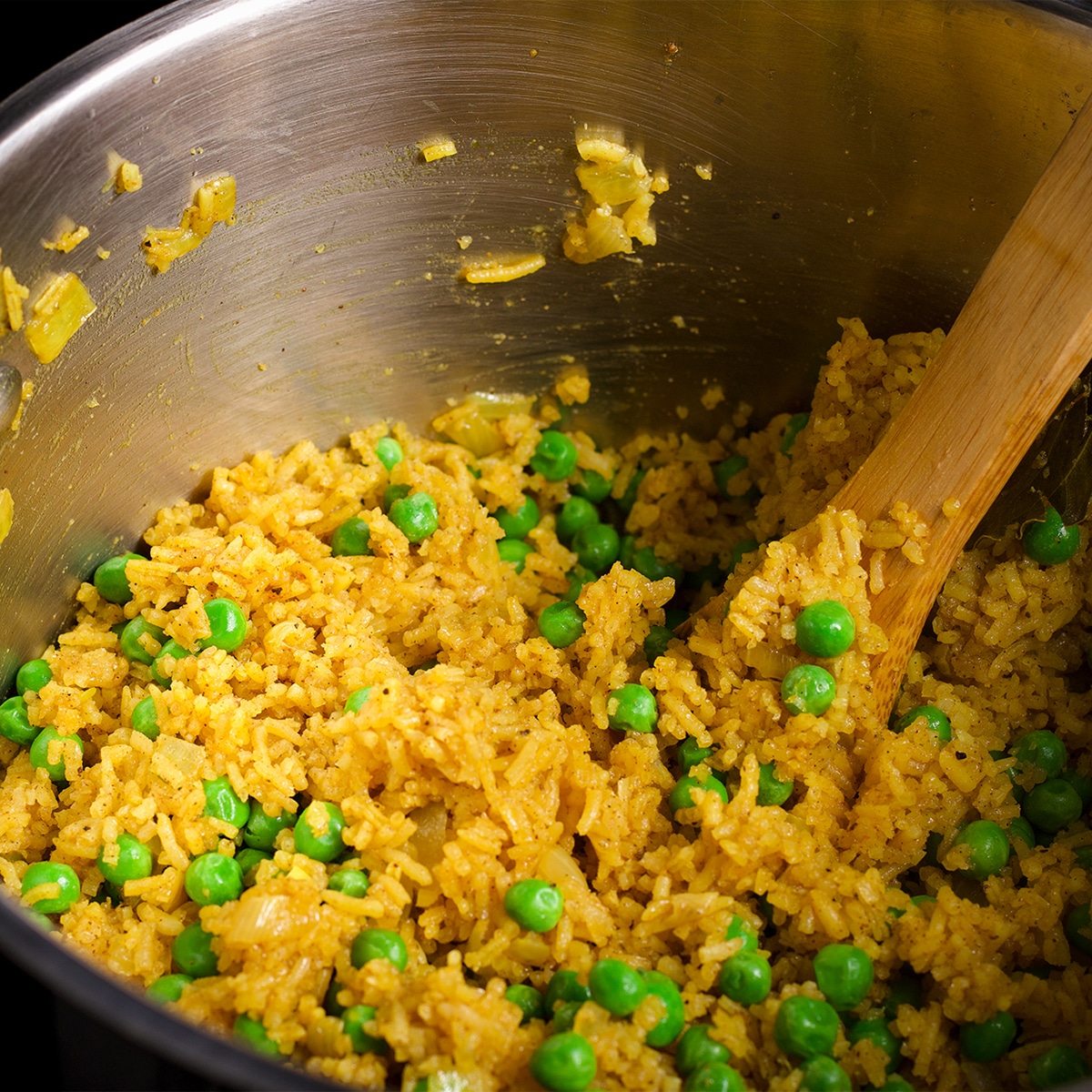 Using a wood spoon to stir peas into cooked Indian Rice.