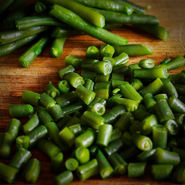A pile of fresh green beans on a wood cutting board. Half the beans are whole and half have been cut into small 1-inch pieces. 