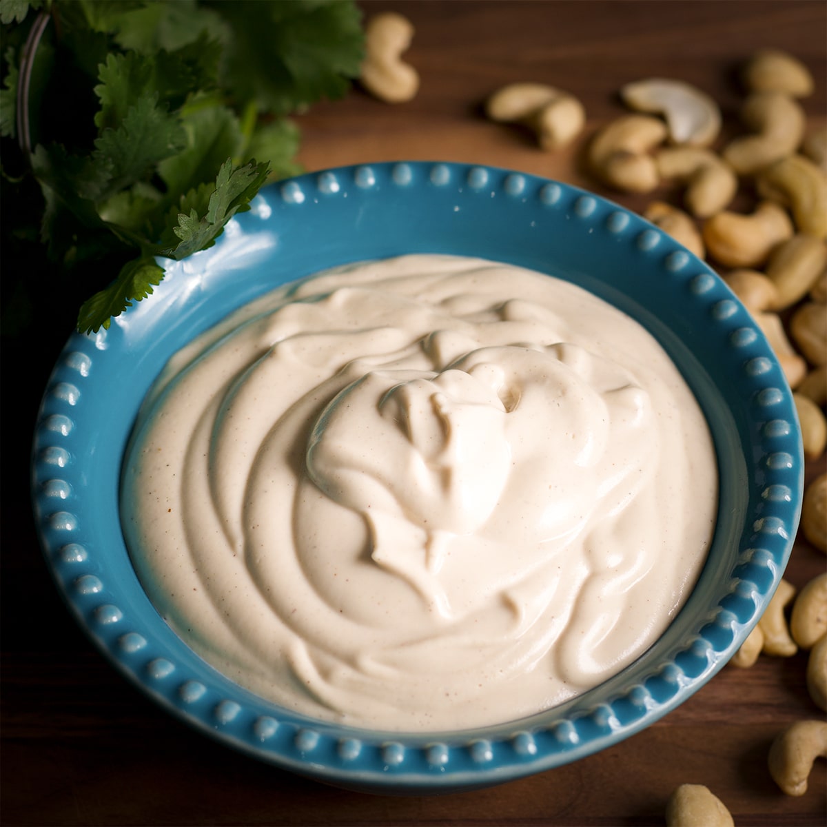 A blue bowl filled with Vegan Sour Cream surrounded by raw cashews.