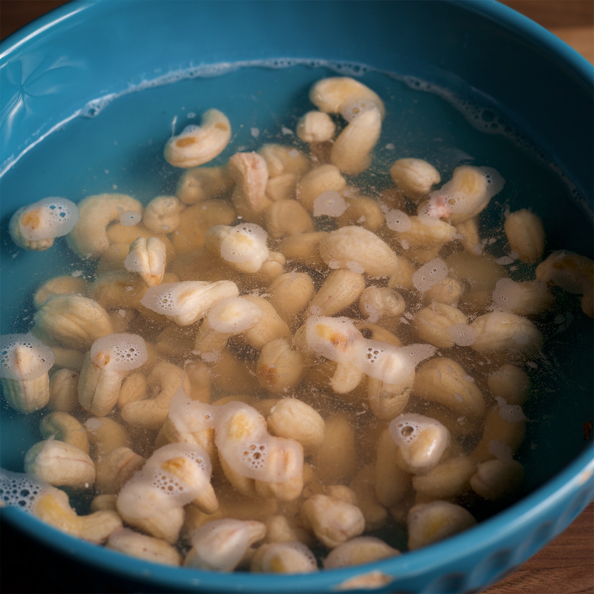 A bowl of raw cashews soaking in hot water.