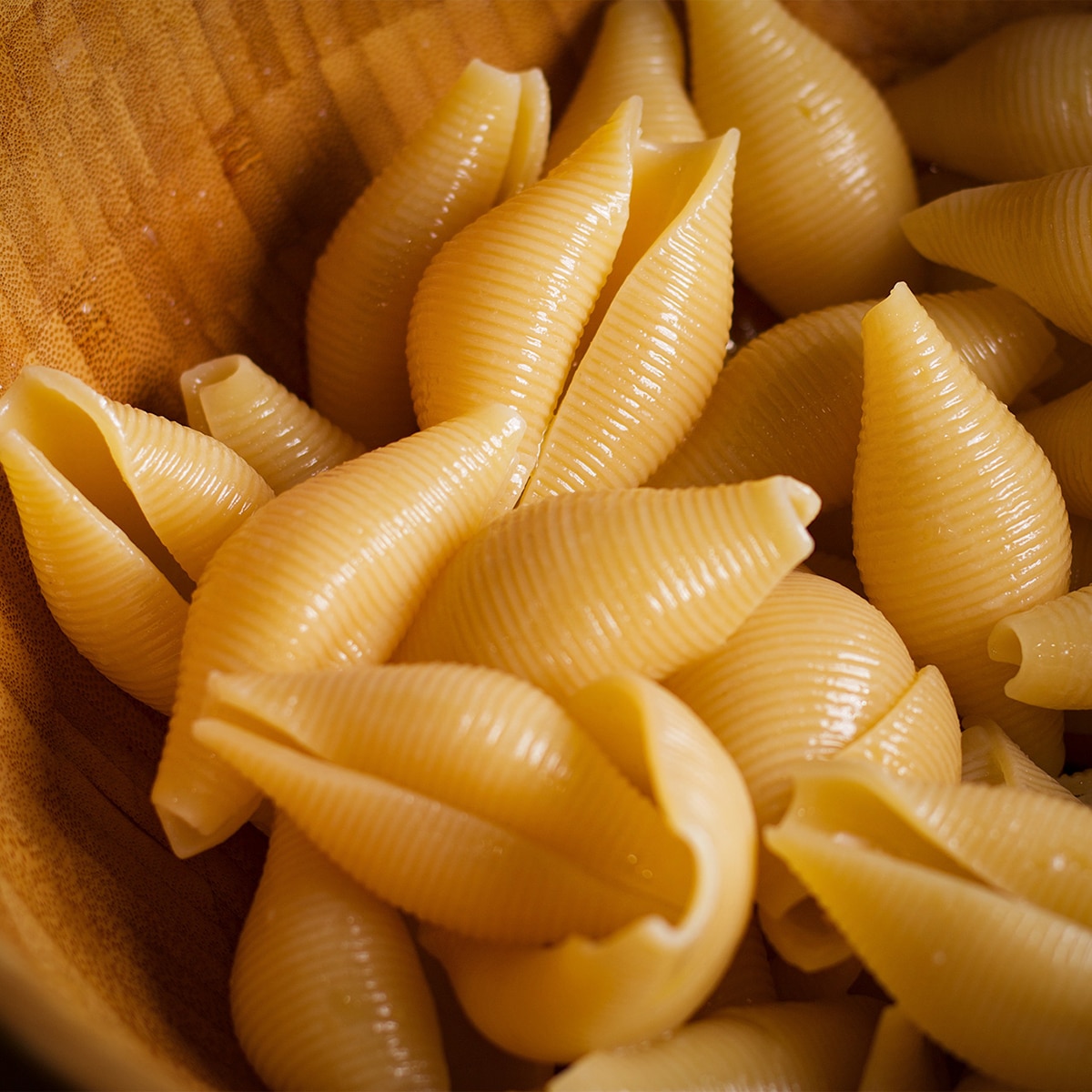 Partially cooked pasta shells cooling in a wood bowl.