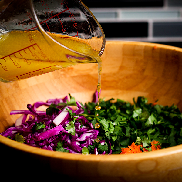 Pouring lime and olive oil vinaigrette over shredded cabbage, carrots, and cilantro to make cilantro cabbage coleslaw.