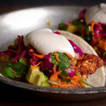 A plate with two Vegan Cauliflower Tacos with avocados, cabbage slaw, and vegan sour cream.