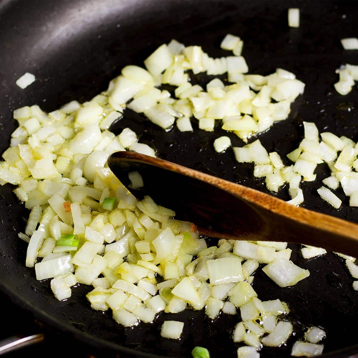 Using a wooden spoon to stir chopped onion as it cooks in a skillet.