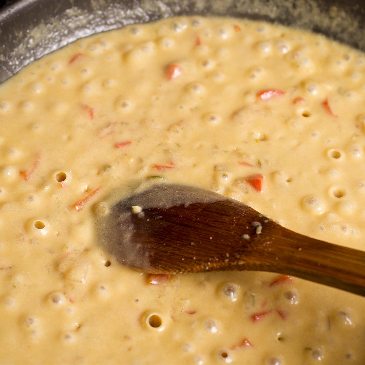 Using a wooden spoon to stir coconut milk and coconut cream into the sauce.