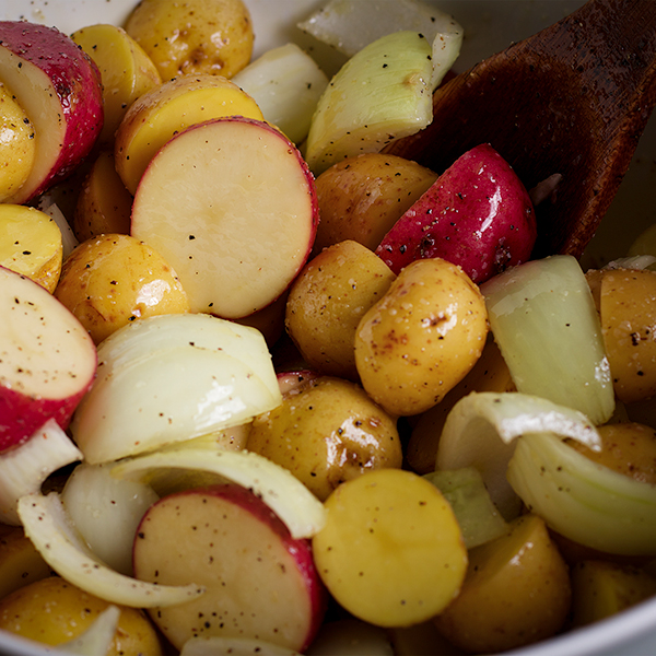 Tossing potatoes, onions, and garlic in a bowl with olive oil and seasoning before adding it to the pan for the Ultimate Sheet Pan Dinner.