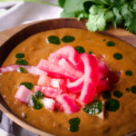 A bowl of black bean soup topped with pickled onions and cilantro oil.
